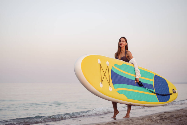 Young woman is carrying paddle board at the beach - Foto, imagen