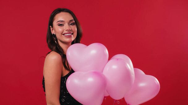happy woman in black dress holding pink balloons isolated on red - Photo, Image