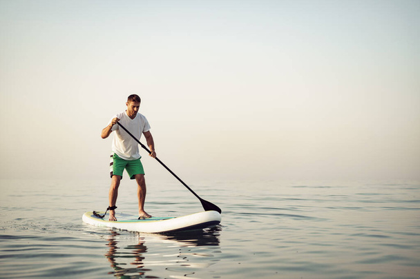 Young man in t-shirt and shorts floating on SUP board - Foto, immagini