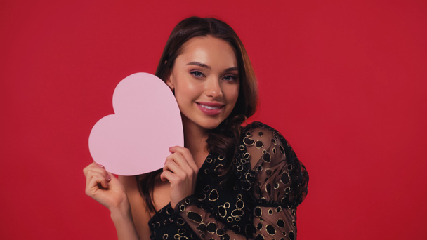 young woman holding paper heart and smiling isolated on red - Foto, Imagem