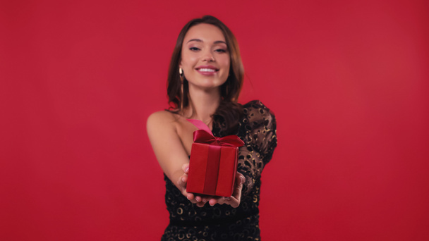 heureuse et floue femme souriant et tenant boîte cadeau sur rouge - Photo, image