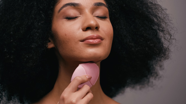 Afroamerykanka używająca silikonowego środka czyszczącego na szyi wyizolowana na szaro - Zdjęcie, obraz