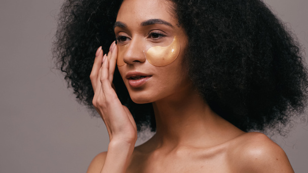 lockige afrikanisch-amerikanische Frau Anwendung Kollagen Augenklappen isoliert auf grau  - Foto, Bild