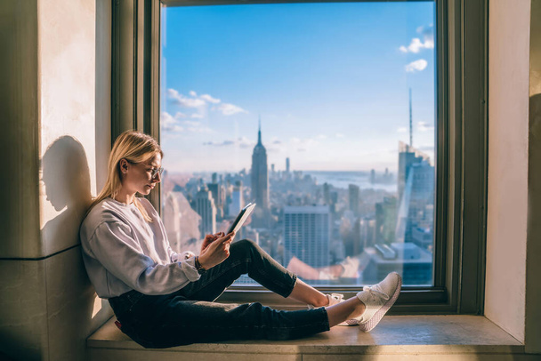 Millennial digital nomad checking booking information during travel journey for visiting New York, youthful female freelancer searching streams website for browsing web content during remote work - 写真・画像