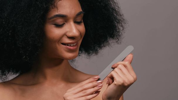 allegra donna afroamericana utilizzando lima per unghie isolato su grigio - Foto, immagini