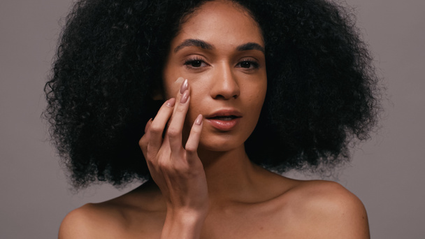 kudrnaté africké americká žena použití obličeje nadace s prsty izolované na šedé - Fotografie, Obrázek