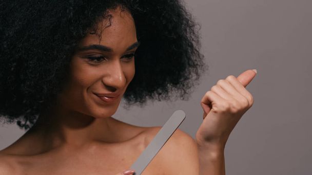 mujer afroamericana positiva usando lima de uñas aislada en gris - Foto, Imagen