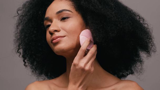 brunette african american woman using silicone cleansing gadget isolated on grey  - Photo, Image