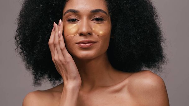 close up de mulher afro-americana aplicando manchas olho hidrogel isolado em cinza - Foto, Imagem