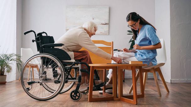 enfermera joven y feliz mujer mayor jugando juego de mesa - Foto, imagen