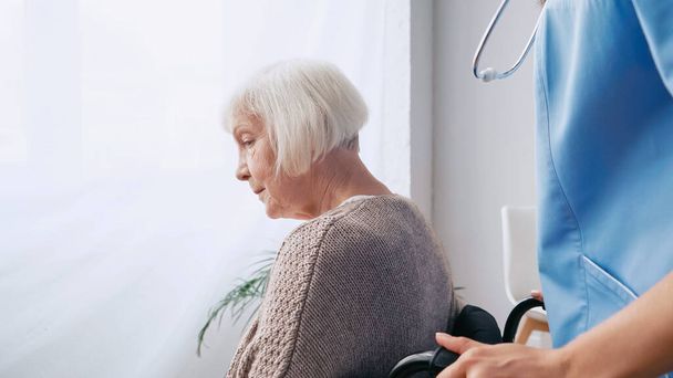 pielęgniarka geriatryczna ze stetoskopem poruszająca starą kobietę na wózku inwalidzkim  - Zdjęcie, obraz