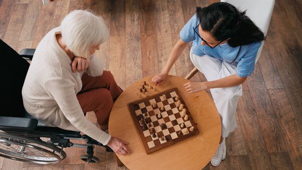 vista superior de anciana y enfermera jugando al ajedrez en el hogar de ancianos - Foto, Imagen