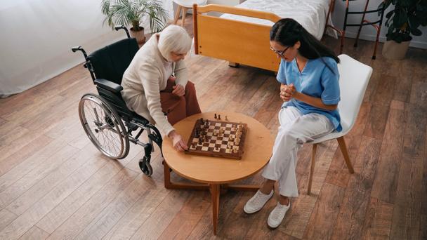 Blick aus der Vogelperspektive auf ältere Frau und Krankenschwester beim Schachspielen im Pflegeheim - Foto, Bild