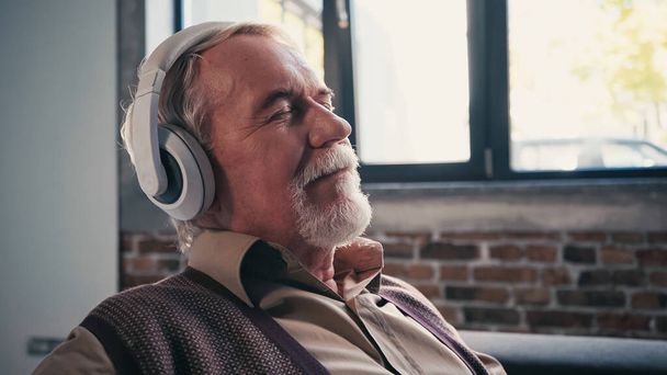tyytyväinen vanhempi mies langattomissa kuulokkeissa kuuntelemassa musiikkia kotona - Valokuva, kuva