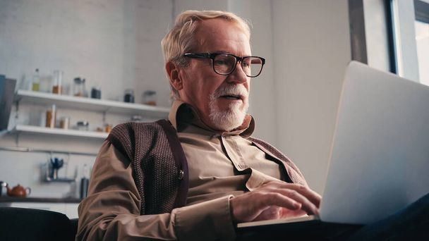 Homme retraité dans les lunettes à l'aide d'un ordinateur portable à la maison - Photo, image