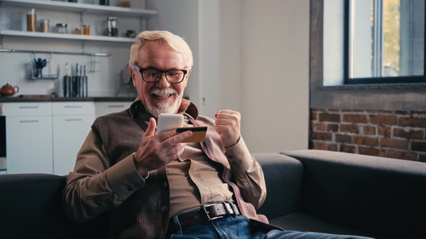 щасливий пенсіонер з кредитною карткою тримає мобільний телефон під час покупок онлайн вдома
 - Фото, зображення