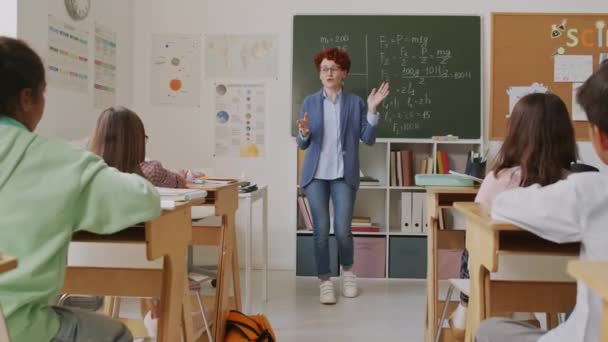 Handheld-Ortung einer fröhlichen Mathelehrerin, die an der Tafel steht und einer Gruppe von Mittelschülern Informationen erklärt - Filmmaterial, Video