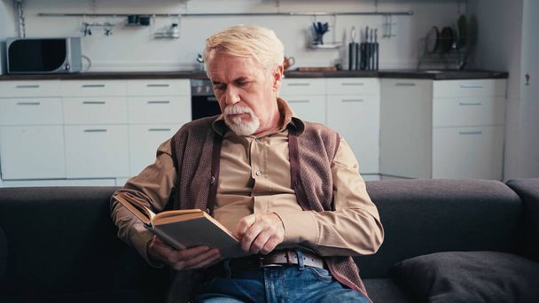 poważne starszy człowiek czytanie książki w domu  - Zdjęcie, obraz