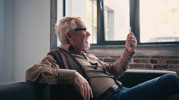 πλαϊνή άποψη του ευτυχούς συνταξιούχου σε γυαλιά έχοντας βιντεοκλήση στο smartphone  - Φωτογραφία, εικόνα