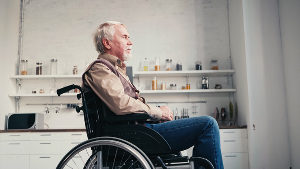 вид сбоку босоногого пенсионера в инвалидной коляске, отводящего взгляд от дома  - Фото, изображение