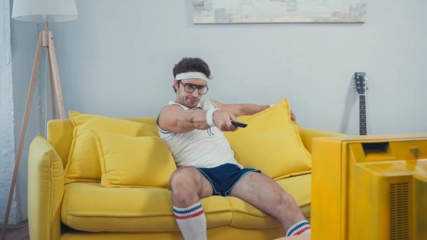 лінивий чоловік у спортивному одязі перемикає канали, сидячи на дивані у вітальні
 - Фото, зображення