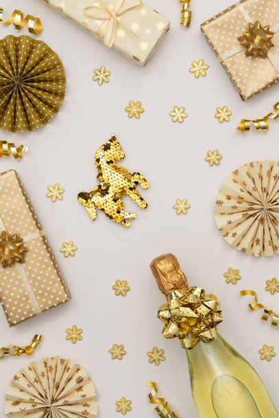 Festlicher Hintergrund mit Goldschmuck, Geschenkschachteln mit einer Flasche Sekt, goldglänzendem Serpentinenkonfetti und Christbaumschmuck aus Papier, glitzernden Schneeflocken und Pferd - Foto, Bild
