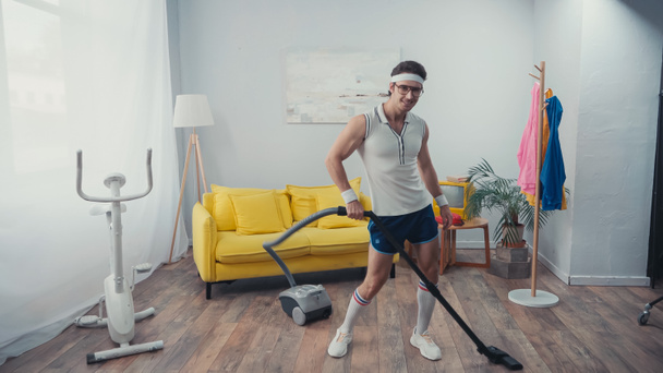 šťastný sportovec tanec při vysávání obývací pokoj, retro sportovní koncept - Fotografie, Obrázek