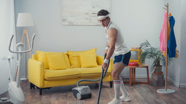 jongeman in sportkleding stofzuiger woonkamer, retro sport concept - Foto, afbeelding