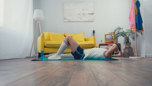 Surface level of sportsman doing abs exercise on fitness mat in living room - 写真・画像