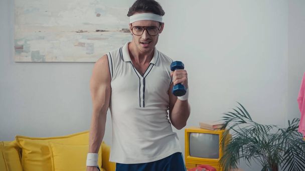 Lustiger Mann beim Gewichtheben im Wohnzimmer, Retro-Sportkonzept - Foto, Bild