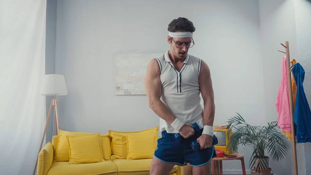 sportsman in eyeglasses exercising with dumbbells in living room, retro sport concept - 写真・画像