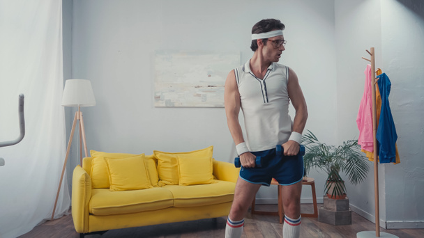 deportista divertido haciendo ejercicio con pesas en la sala de estar, concepto de deporte retro - Foto, Imagen