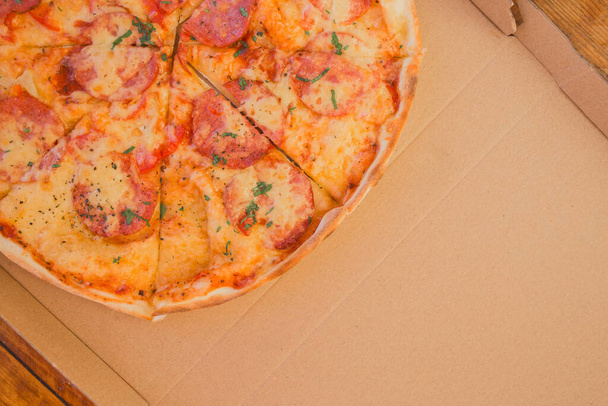 Fresh cheese pizza with salami sausage cut on the cardboard background of the box. - Foto, immagini