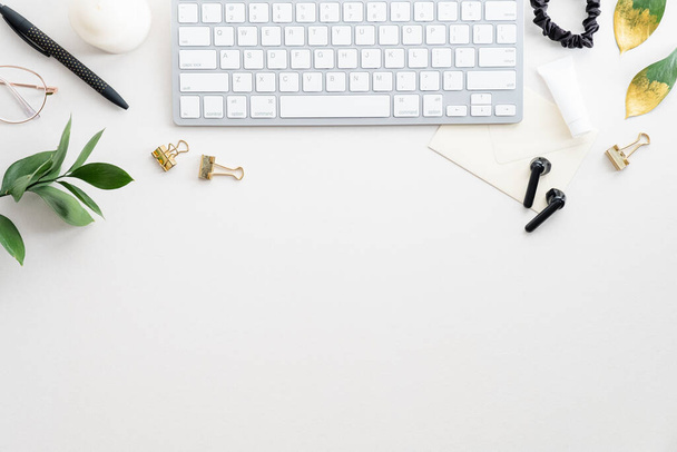 Elegant feminine workspace with keyboard, green leaves, candle, earphones on white background. Home office desk table top view, flat lay. - Fotó, kép