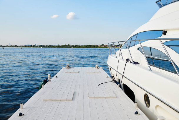 Bílá luxusní moderní jachta kotvící poblíž bílého dřevěného mola. Loď před vyplutím. - Fotografie, Obrázek