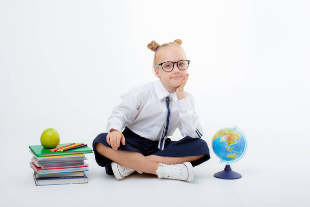 a little schoolgirl girl in a school uniform is sitting isolated on a white background - Φωτογραφία, εικόνα