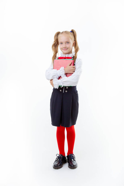 une petite écolière en uniforme scolaire tient un livre isolé sur fond blanc - Photo, image