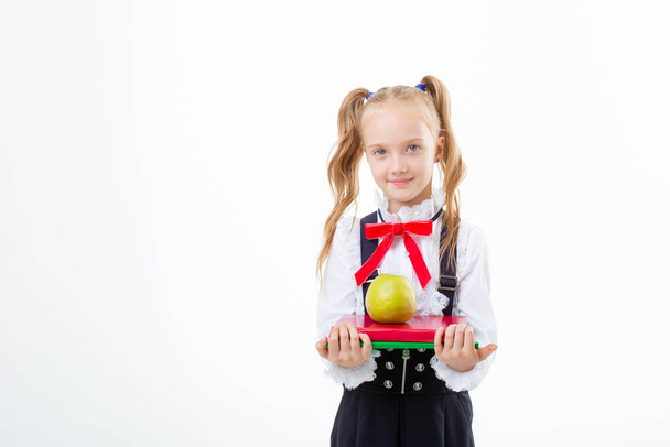 una niña con uniforme escolar sostiene un libro y una manzana aislada sobre un fondo blanco - Foto, Imagen