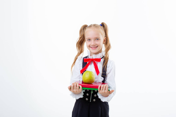 una bambina in uniforme scolastica tiene un libro e una mela isolata su uno sfondo bianco - Foto, immagini