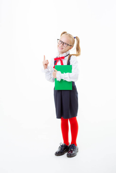 mała uczennica dziewczyna w szkolnym mundurku trzyma książkę na białym tle - Zdjęcie, obraz