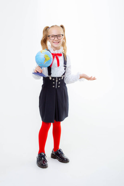 Маленька школярка у шкільній формі тримає на білому фоні земну кулю. - Фото, зображення