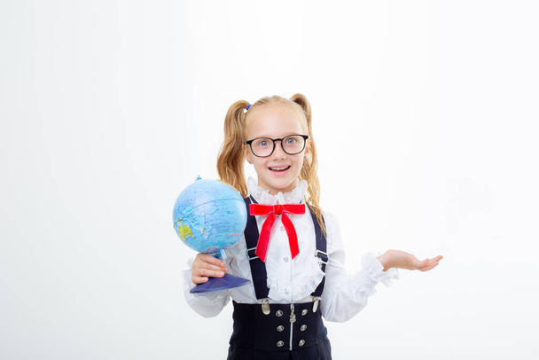 a little schoolgirl girl in a school uniform holds a globe isolated on a white background - Фото, изображение