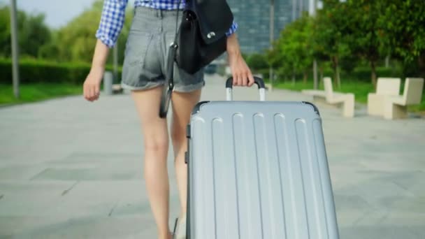 női lábak sétálnak a járdán, és egy bőröndöt cipelnek maguk mögött.. - Felvétel, videó