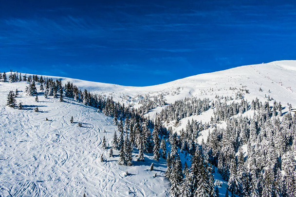 zimowy krajobraz w górach na tle błękitnego nieba. Ośnieżone drzewa świecące pod słońcem. stok narciarski i szlak - Zdjęcie, obraz