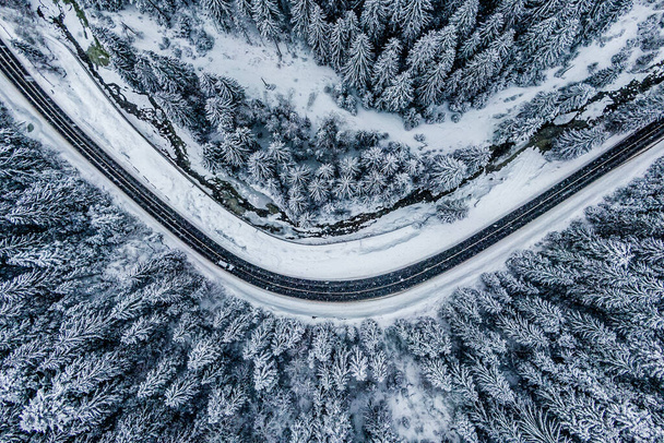 solo coche blanco conduciendo por carretera de asfalto a través de las montañas de invierno en la nieve. Drone vista superior del bosque de invierno congelado - Foto, Imagen