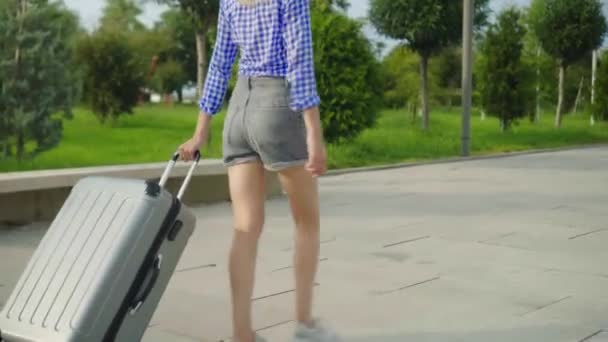 Τα πόδια των γυναικών περπατούν στο πεζοδρόμιο και κουβαλάνε μια βαλίτσα πίσω τους.. - Πλάνα, βίντεο