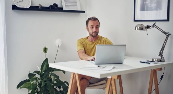 Дорослий білий чоловік працює на ноутбуці вдома
. - Фото, зображення