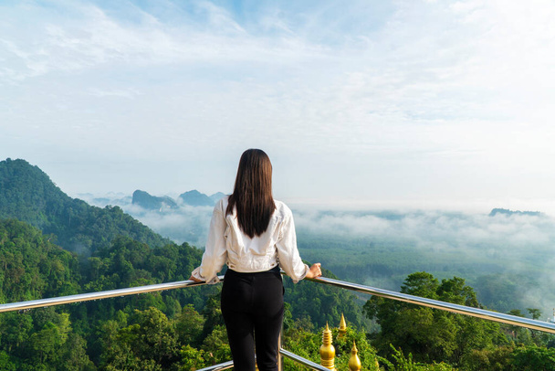 Kalandtúra nyaralás koncepció. Vissza a fiatal utazó nő áll a hegy tetején kilátást erdő és köd élvezze a napfény reggel Thaiföldön. - Fotó, kép