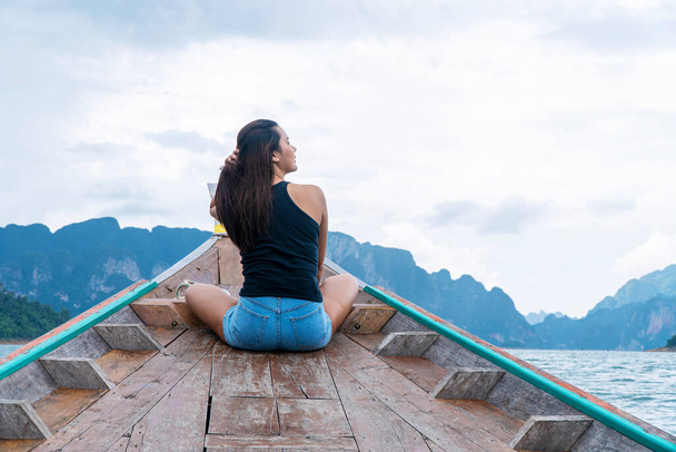 Przygoda styl życia urlopowicz relaks koncepcja. Podróżnik młoda kobieta trzyma własne włosy siedząc na długi ogon łodzi pływające laguny z górami i niebem podczas wakacji turysta w Surat Thani. - Zdjęcie, obraz