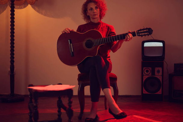 Kobieta gra na gitarze akustycznej w pokoju retro vintage. - Zdjęcie, obraz